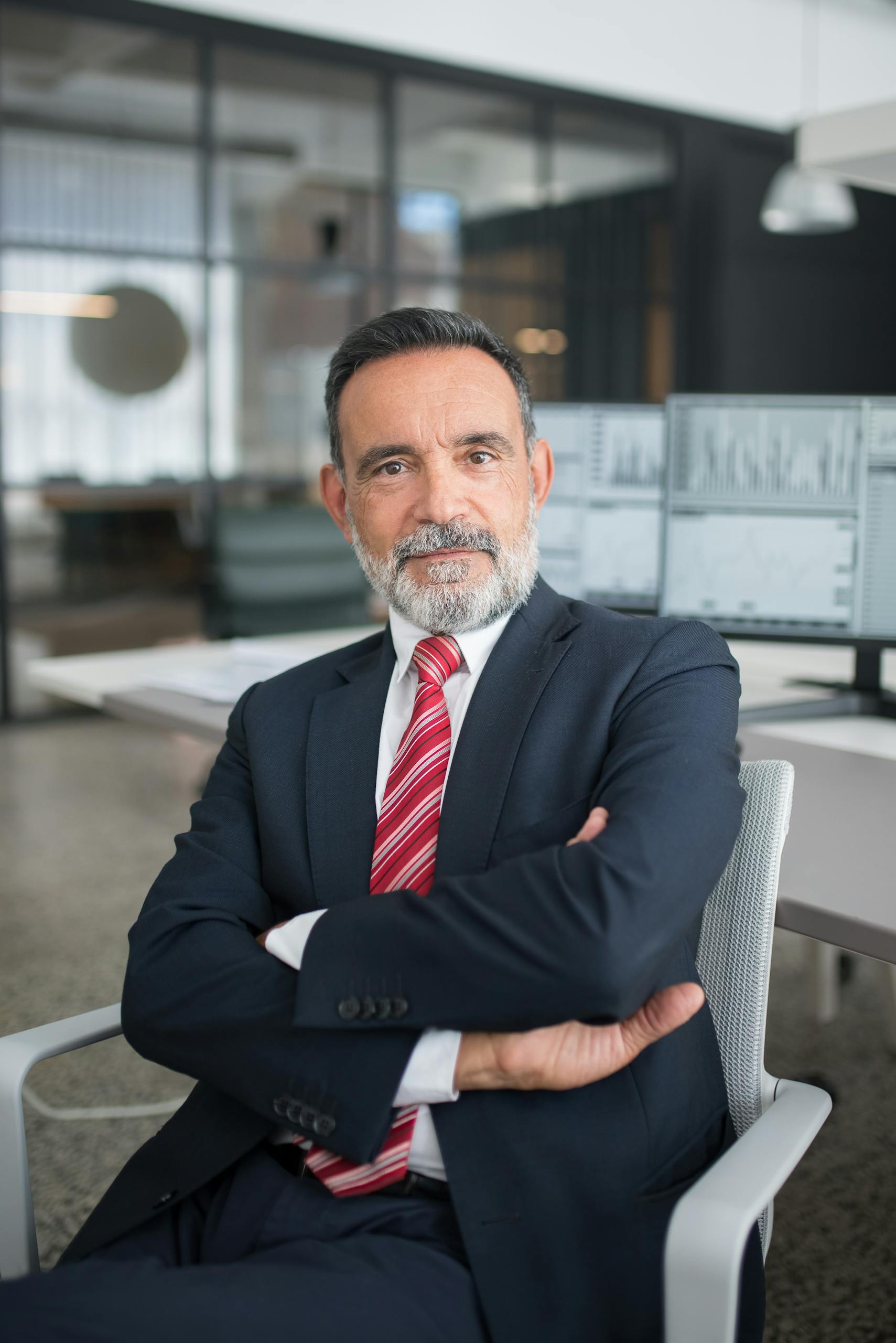 Professional businessman sitting confidently in a modern office with multiple screens displaying data.